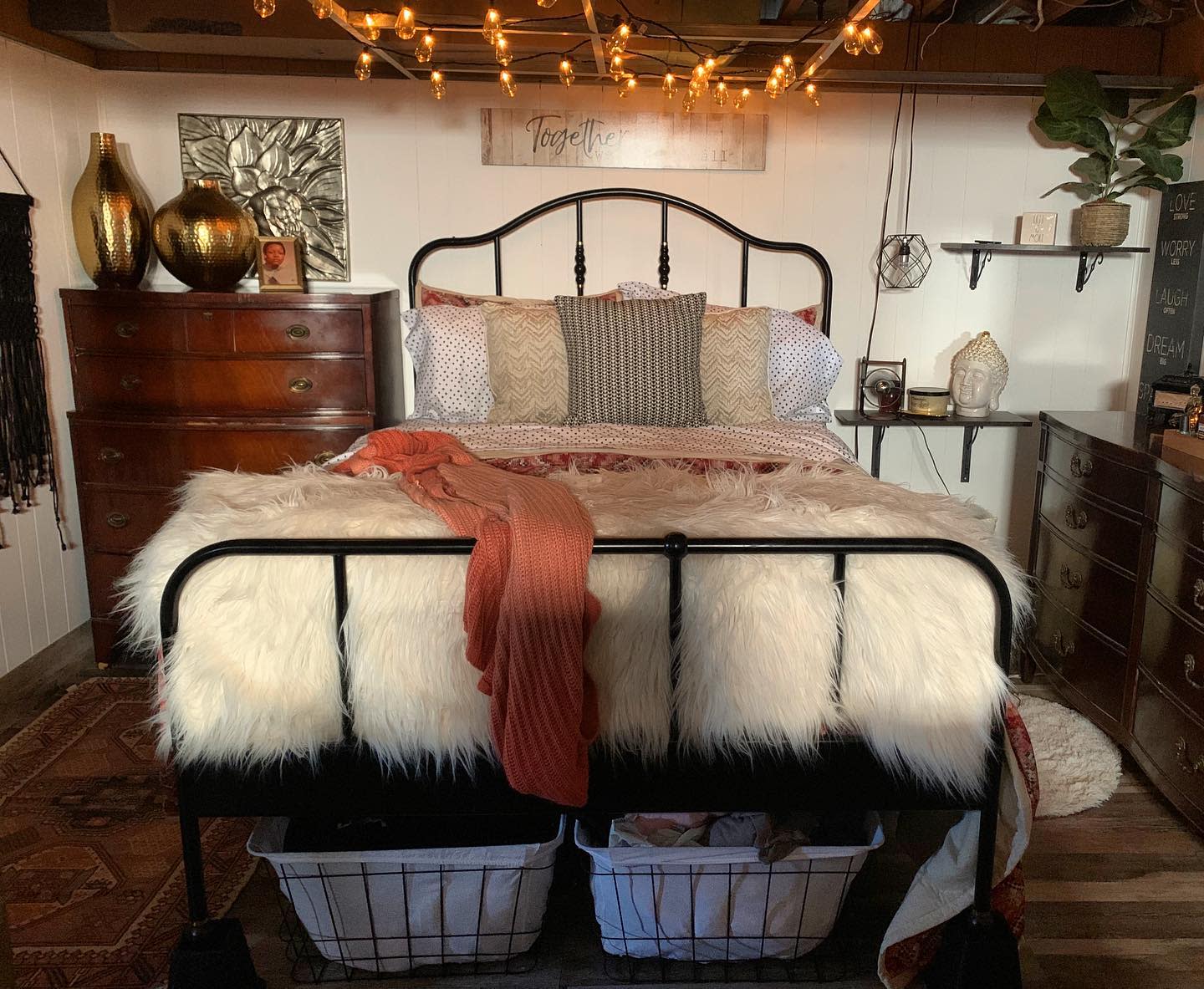 Cozy bedroom with string lights, metal bed frame, fluffy blanket, and wooden dressers.